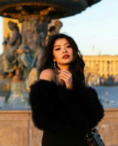 a woman standing in front of a fountain wearing a black dress and fur stoler