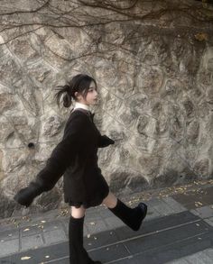 a woman in black coat and boots walking on sidewalk