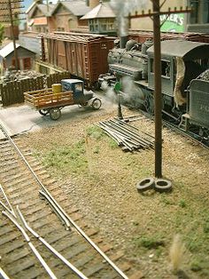 an old fashioned train is on the tracks near other model railroad tracks and buildings in the background