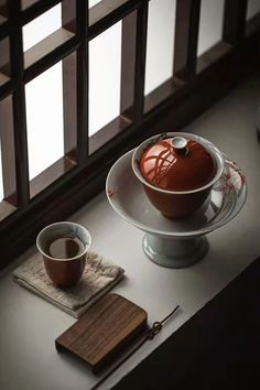 a bowl and cup on a plate with chopsticks next to it in front of a window