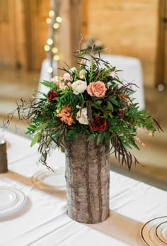 an arrangement of flowers in a wooden vase on a table with plates and napkins