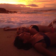 two women laying on the beach at sunset