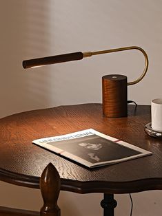 a wooden table with a magazine, coffee cup and lamp on it