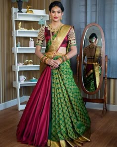 a woman standing in front of a mirror wearing a green and red sari with gold accents