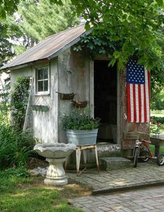 an old outhouse with a flag on the door and potted plants in front