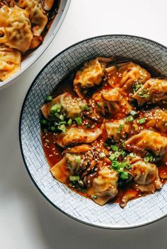 two bowls filled with dumplings and sauce on top of a white table next to each other