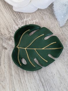 a large green leaf shaped brooch with gold trimmings on a wooden surface