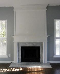 an empty living room with gray walls and white trim on the fireplace mantels