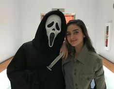 a woman standing next to a person in a ghost costume with a knife sticking out of it's mouth