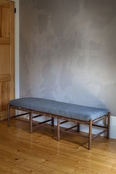 a wooden bench sitting on top of a hard wood floor next to a gray wall