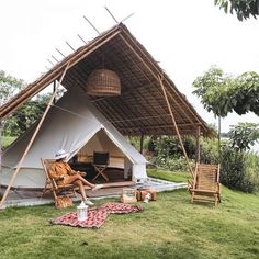 a large tent with a thatch roof next to a body of water in the background