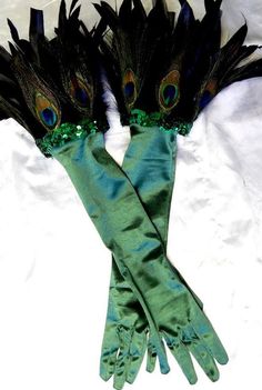 two green gloves with peacock feathers on them sitting on top of a white cloth covered bed