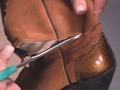 a person cutting the side of a brown shoe with a pair of blue handled scissors