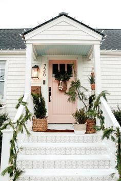 a white house with potted plants on the steps and a pink door in front