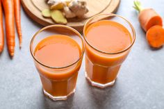 two glasses filled with carrot juice next to sliced carrots