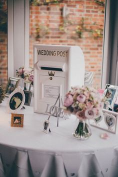 a white table with flowers and pictures on it in front of a brick wall that says wedding post