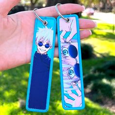 two key chains with anime characters on them are held in the palm of a person's hand