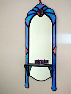 a stained glass mirror hanging on the wall next to a shelf with two candles in it