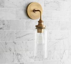 a light fixture on the wall in a bathroom with marble walls and white tiles behind it