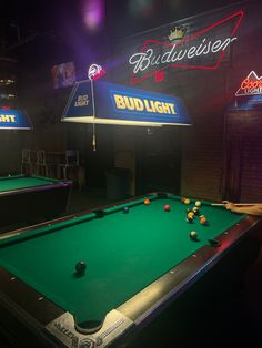 two pool tables with balls on them in front of a budweiser neon sign