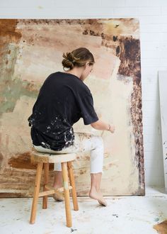 a woman sitting on top of a stool in front of a painting