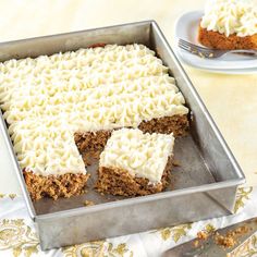 carrot cake with white frosting in a pan on a table next to a fork