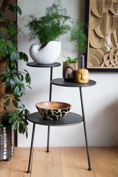 two black and white bowls are sitting on three tiered stands in front of a plant