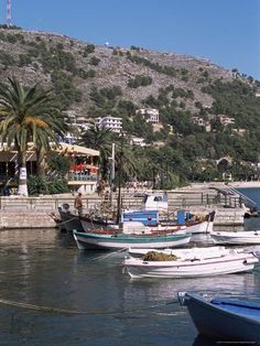 several boats are docked in the water near some hills and buildings on top of a hill