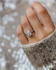 a woman's hand with a diamond ring on her finger, in front of silver sequins