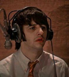 a man wearing headphones and a tie in front of a microphone with his mouth open