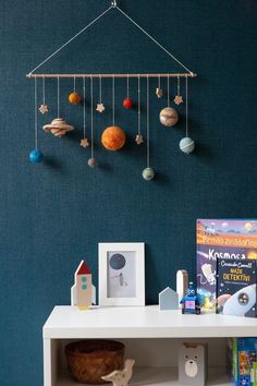 a space themed mobile hangs on the wall next to a shelf with books and toys