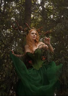 a woman with red hair wearing a green dress in the middle of a forest surrounded by trees