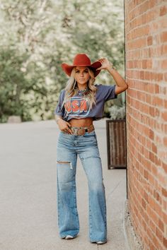 Calling all denim lovers, your new favorite jeans have arrived! The Jules Wide Leg Jeans are stretch denim with distressed detailing and a high rise wide-leg fit. We’ve paired it with our Neon Cowboy Hat Graphic Tee and a statement belt for a classic stockyard fit! Wide Leg Jeans And Tshirt Outfit, Cowboy Hat Women Outfit, Cute Western Concert Outfits, Western Wide Leg Jeans Outfit, Boho Cowgirl Outfits, All Denim Look, Grunge Country Outfit, Cute Cowgirl Outfits Rodeo, Outside Concert Outfit Summer