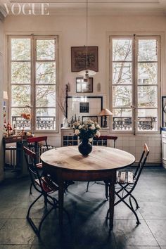 a dining room table and chairs in front of three windows with potted flowers on them