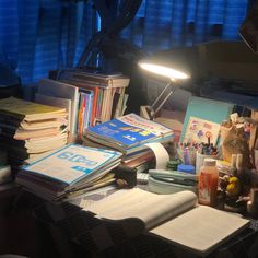 a cluttered desk with many books and papers on it, lit by a lamp