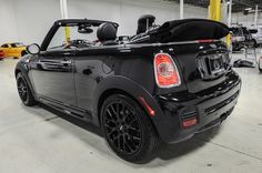 the back end of a black convertible car parked in a garage with other cars behind it