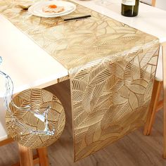 a white table with a gold leaf design on it and a bottle of wine next to it