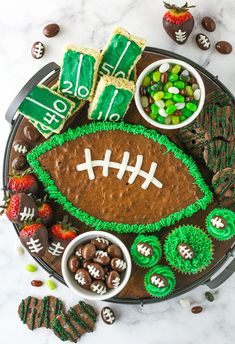 a football shaped cake with green frosting and chocolate candies around it on a platter