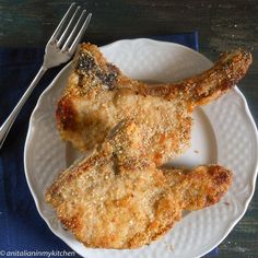 two pieces of fried chicken on a white plate with a fork and knife next to it