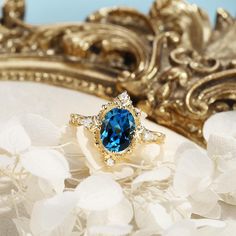 a blue ring sitting on top of white flowers next to a gold frame and mirror