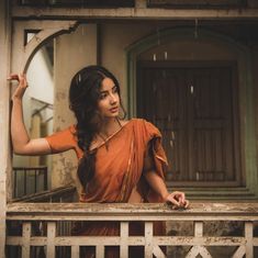 a woman in an orange sari standing on a porch with her arms behind her head