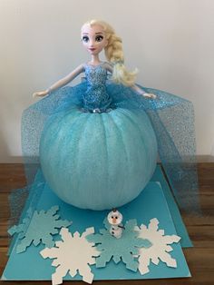 a frozen princess doll sitting on top of a blue pumpkin with snowflakes around it