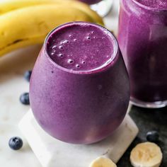 two glasses filled with blueberry smoothie next to bananas