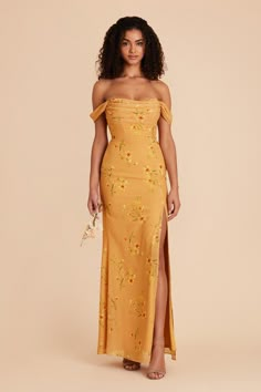 a woman wearing an off the shoulder yellow dress with floral embroidery on it and side slit