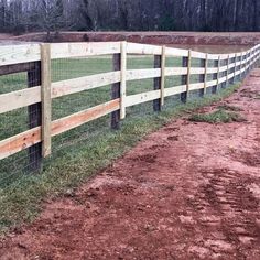 a wooden fence with wire around it on the side of a dirt road next to a field