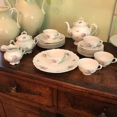 a table topped with lots of white dishes and vases next to a wooden dresser