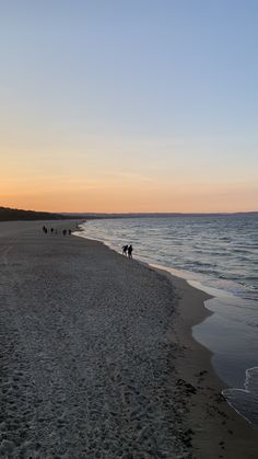 people are walking along the beach at sunset