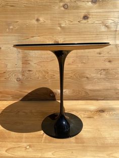 an oval table with a black base on a wooden floor in front of a wood paneled wall