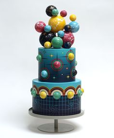 a three tiered cake decorated with colorful balls and stars on the top, sitting on a metal stand