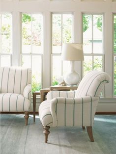 a living room with two chairs and a lamp on the side table in front of large windows